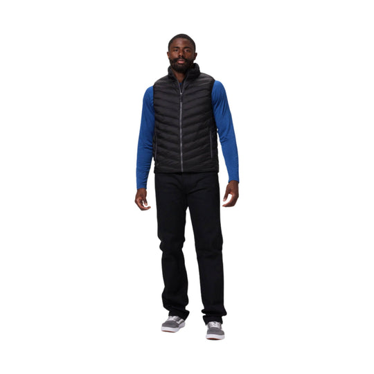 Black quilted zip-front heated vest worn over a blue long-sleeve shirt, shown with black pants and gray sneakers