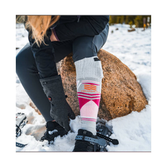 Knee-high heated sock with pink and gray stripes worn over a snowboard boot in the snow