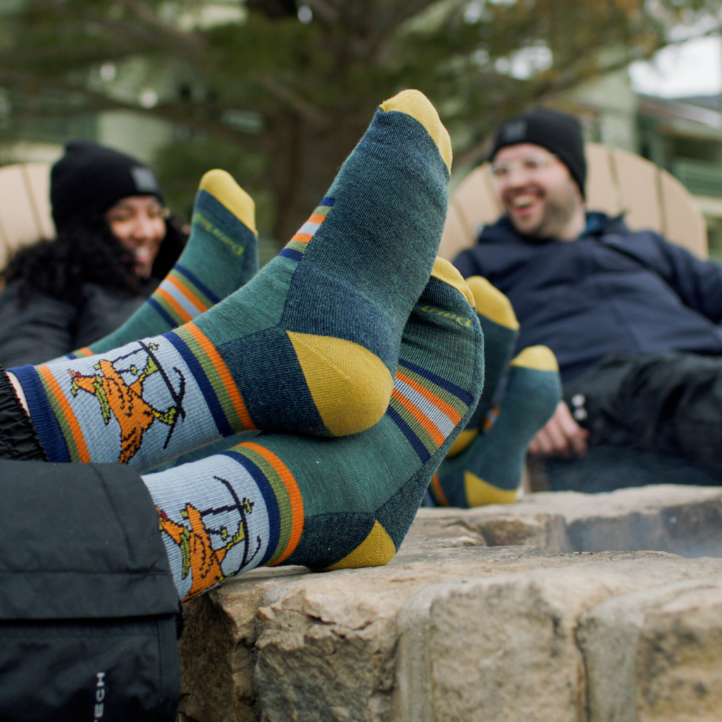 Two people sitting outdoors with colorful patterned socks on, one person is wearing a black jacket and the other is wearing a blue jacket.