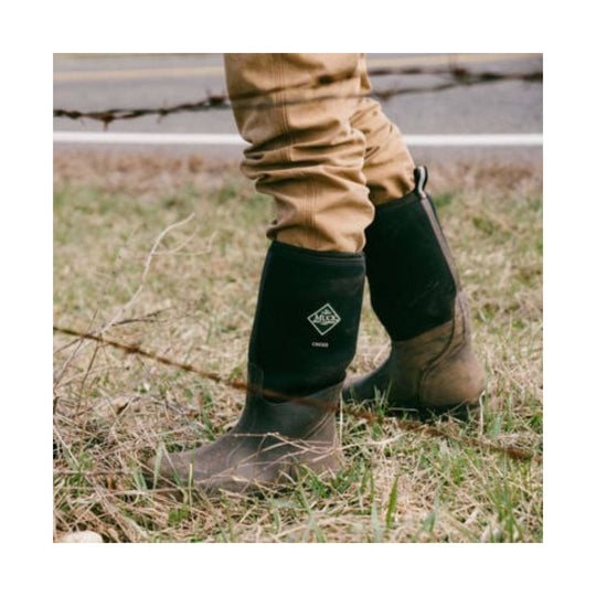 Black and tan pull-on rubber work boots with logo on the shaft, shown outdoors on grass