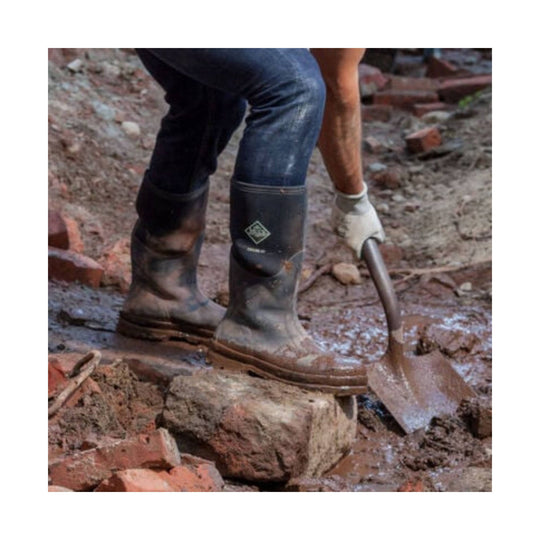 Mud-covered black knee-high work boots on a muddy construction site
