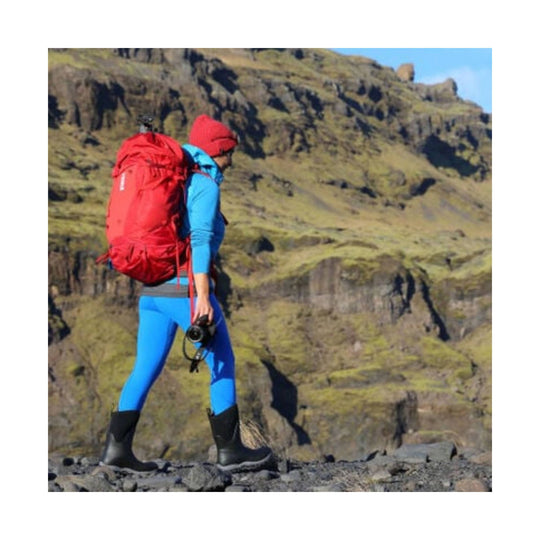 Black mid-height insulated rubber boots worn with blue leggings on rocky ground