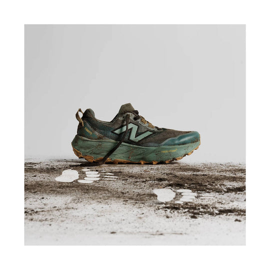 Mud-covered trail running shoe in dark green and black with a large side logo and rugged outsole