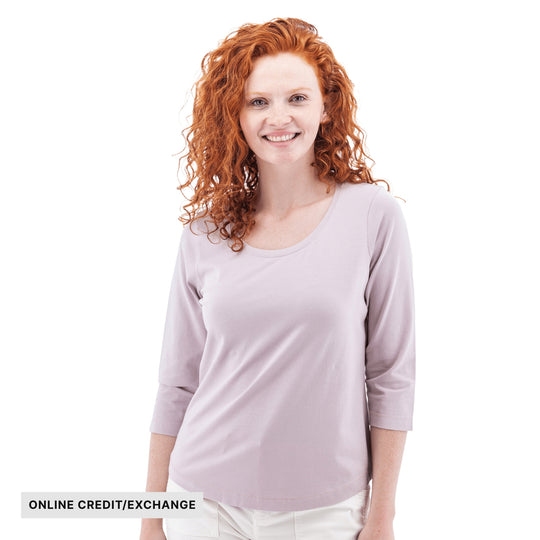 Woman wearing a light lavender three-quarter sleeve top with visible text "ONLINE CREDIT/EXCHANGE"