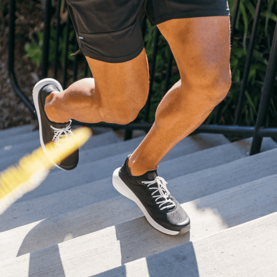 Black low-top running shoe with white sole and white laces, worn while going down concrete steps