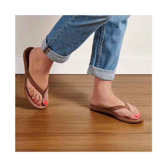 Brown leather thong sandals on a person wearing cuffed jeans