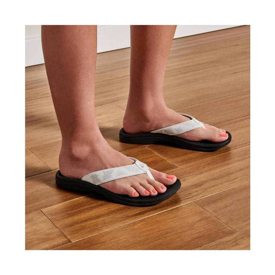 Pair of white thong sandals with black soles on a wood floor