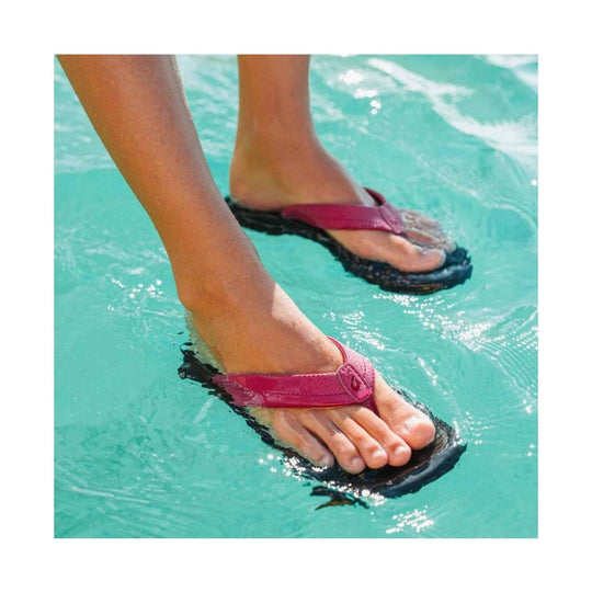 Pink thong sandals with black soles worn in shallow water