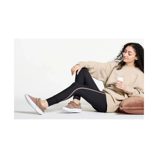 Taupe slip-on shoes with fuzzy trim and thick white soles worn with black leggings