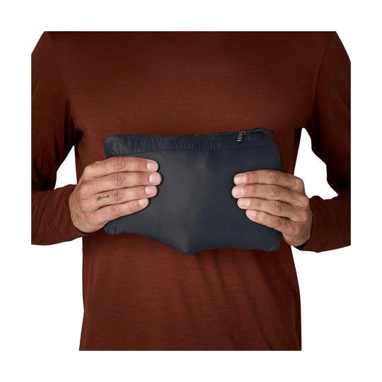 Hands holding a compact dark navy puffer jacket in a zippered pouch