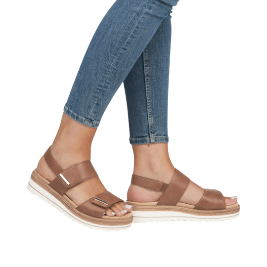 Brown strappy platform sandals with white soles, shown on feet with cropped blue jeans