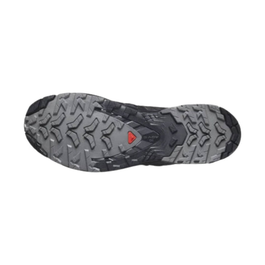 Grey and black trail shoe outsole with aggressive lug tread and a small red triangular logo