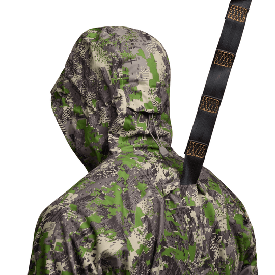 Camouflage hooded jacket with a black webbing strap showing repeated SITKA text