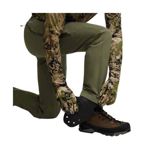 Olive green pants on a kneeling model with camo gloves and a brown-and-black hiking boot