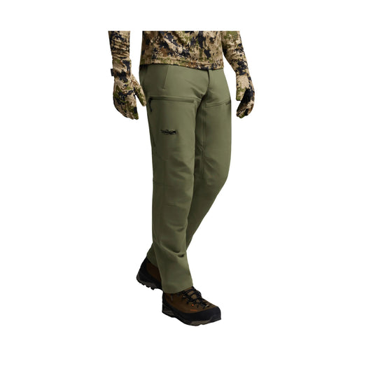 Olive green technical hiking pants with zip thigh pocket, shown on a model with camo top and gloves