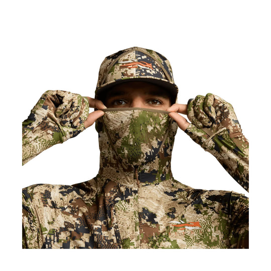 Camouflage hooded face covering jacket with matching cap and gloves, worn by a model pulling up the face mask