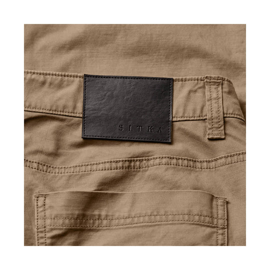 Close-up of tan cargo pants with a black leather patch labeled SITKA