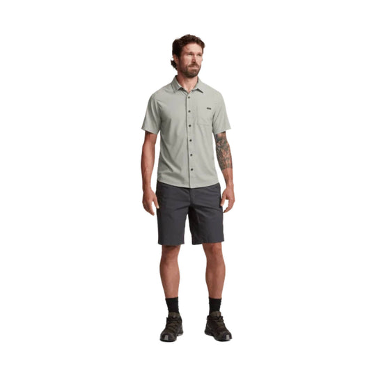 Light gray short-sleeve button-up shirt with chest pocket, shown on a model with dark shorts and hiking shoes