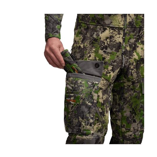 Camouflage cargo bib pants with zip fly, side pocket flap, and a hand holding a folded camouflage item