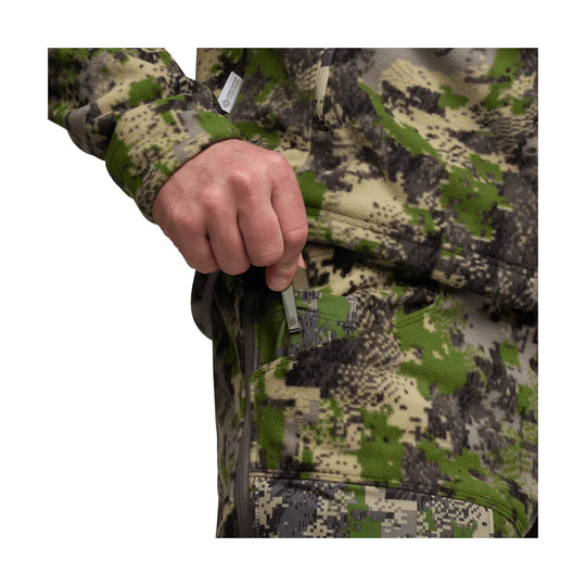Camouflage fleece pant with a zippered thigh pocket, shown on a model's torso and hand