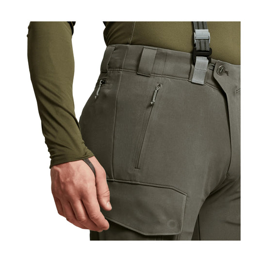 Olive technical hiking pants with suspenders, zip thigh pockets, and a reinforced cargo flap