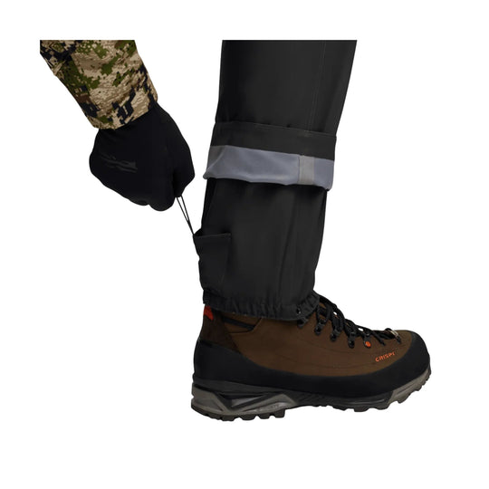 Brown-and-black hiking boot with rugged sole and black gaiter, shown on a pant leg