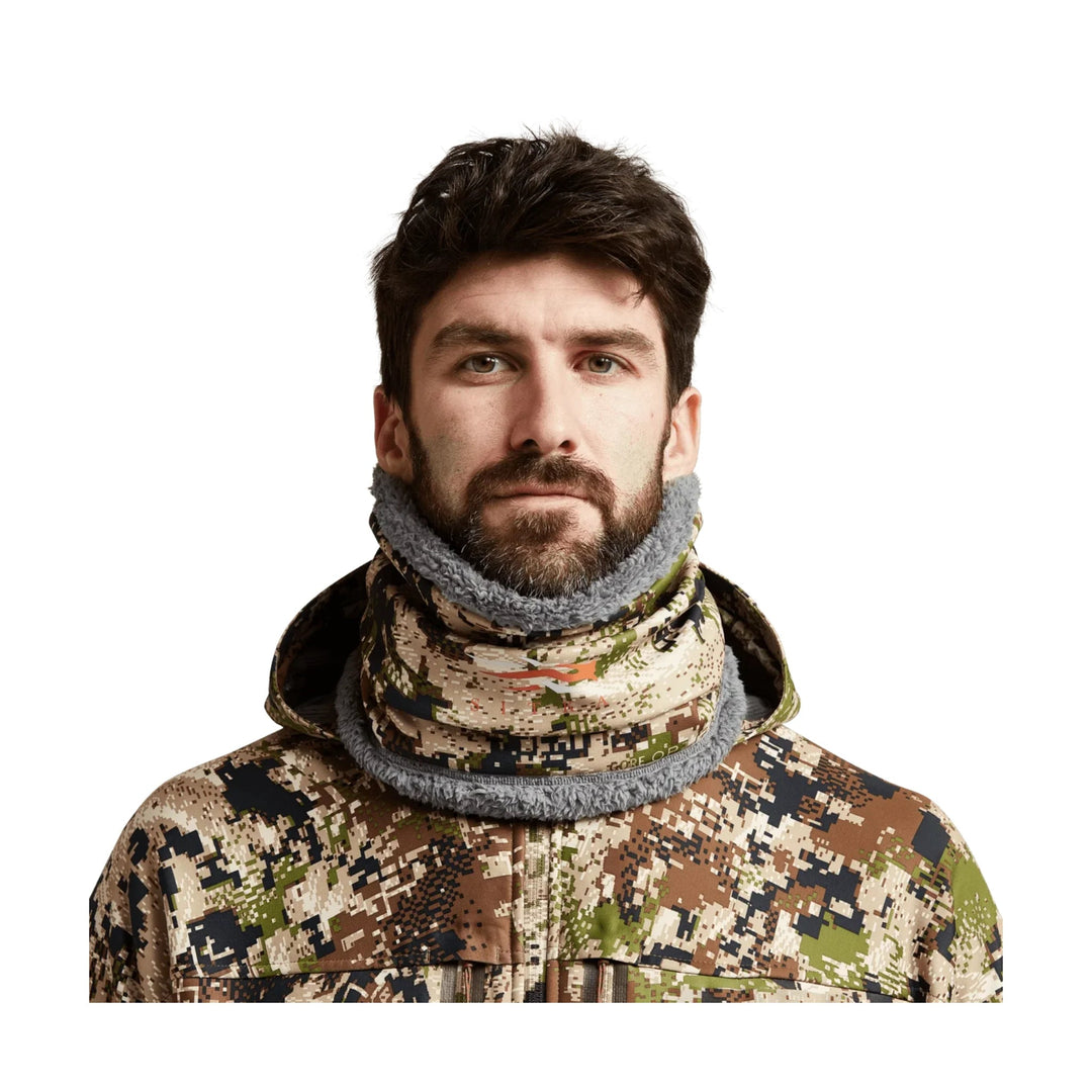 Camouflage neck gaiter worn over the neck and lower face with a hooded camouflage jacket