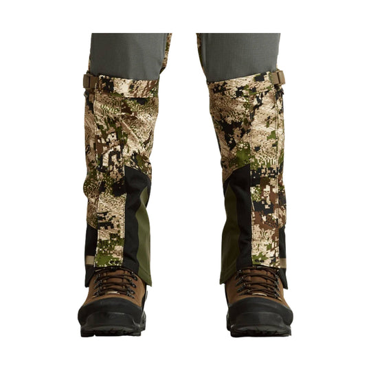 Camouflage gaiters over brown hiking boots on a pair of legs