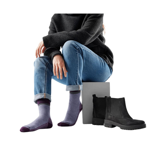Light purple crew socks with darker purple heel and toe on a model seated beside black ankle boots
