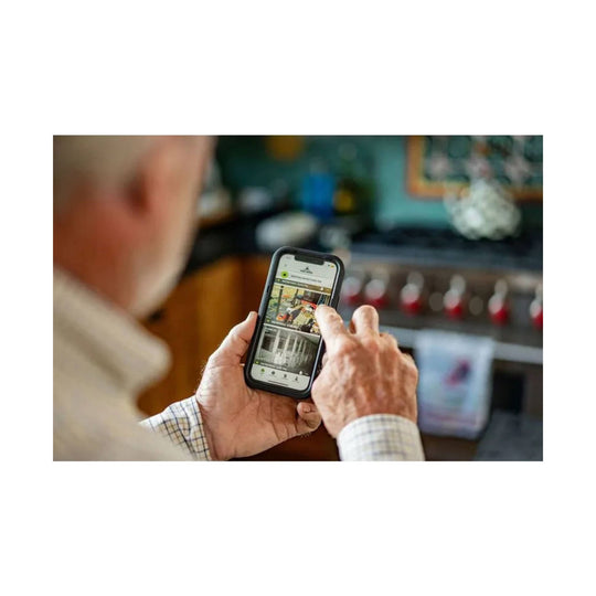 Person holding a smartphone showing a security camera app in a kitchen