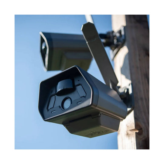Black security camera mounted on a wall bracket against a blue sky