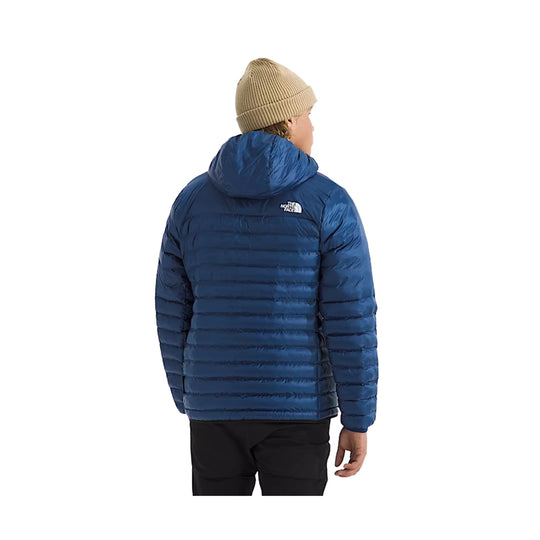 Blue hooded puffer jacket shown from the back with a small chest logo and black pants