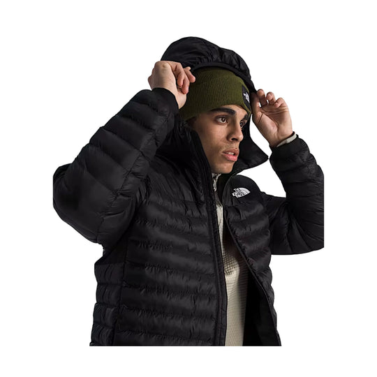Black hooded puffer jacket worn over an olive knit beanie, shown in side profile