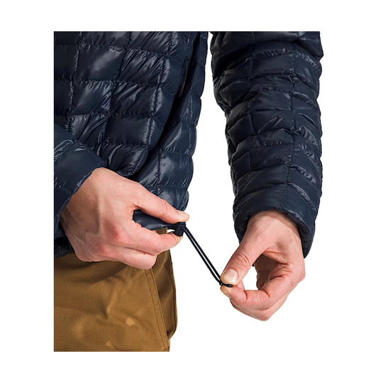 Navy quilted puffer jacket with front hem drawcord being tightened by hand