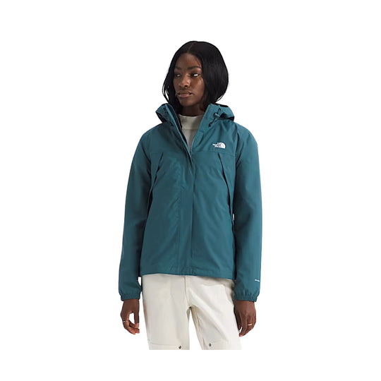 Teal hooded zip-up jacket with chest logo, worn over a light sweater and white pants