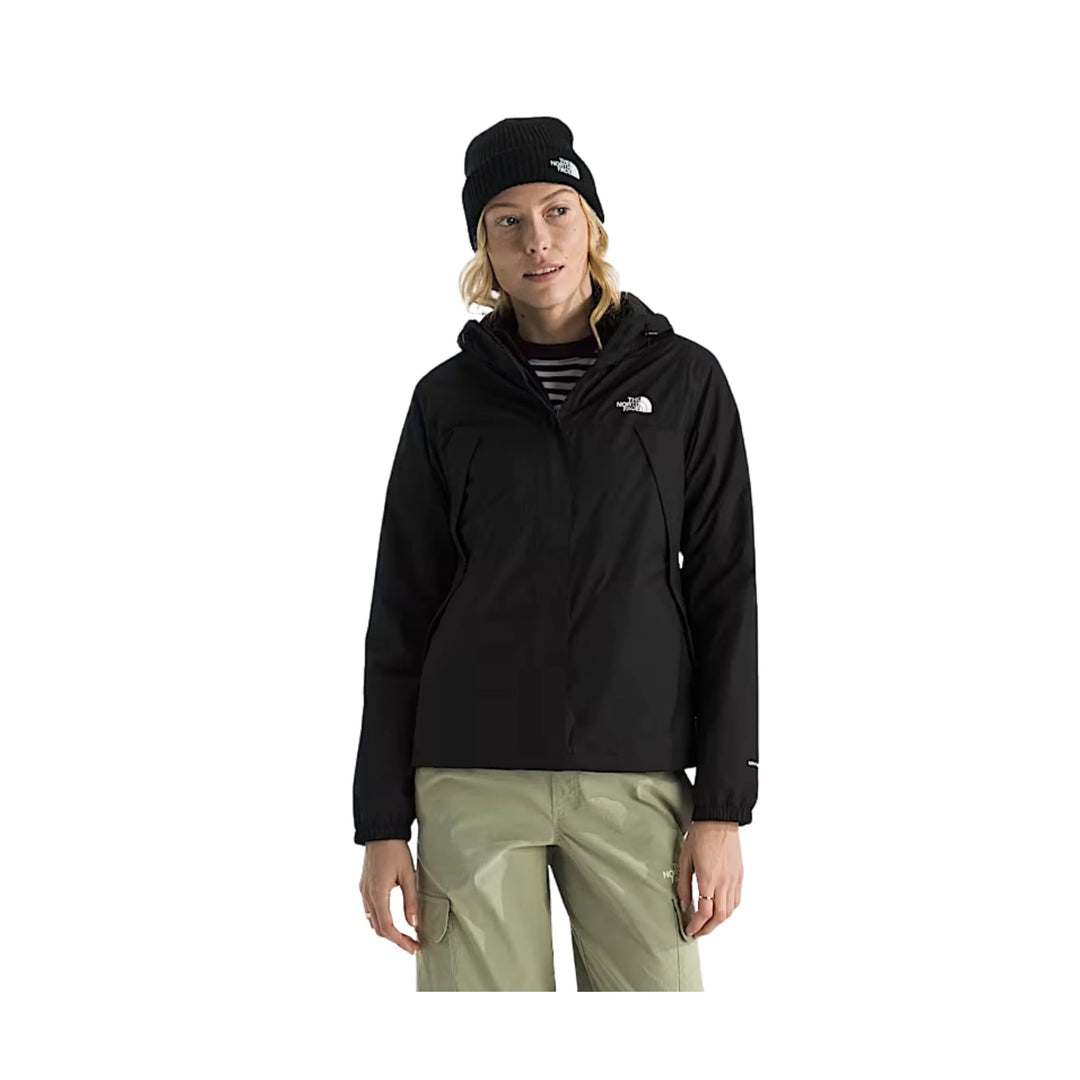 Black hooded jacket with a small white chest logo, worn over a striped top and paired with light cargo pants