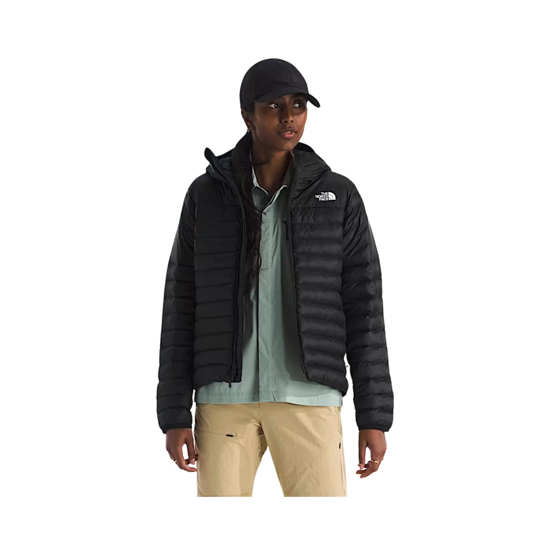 Black puffer jacket with hood, worn open over a light shirt and tan pants