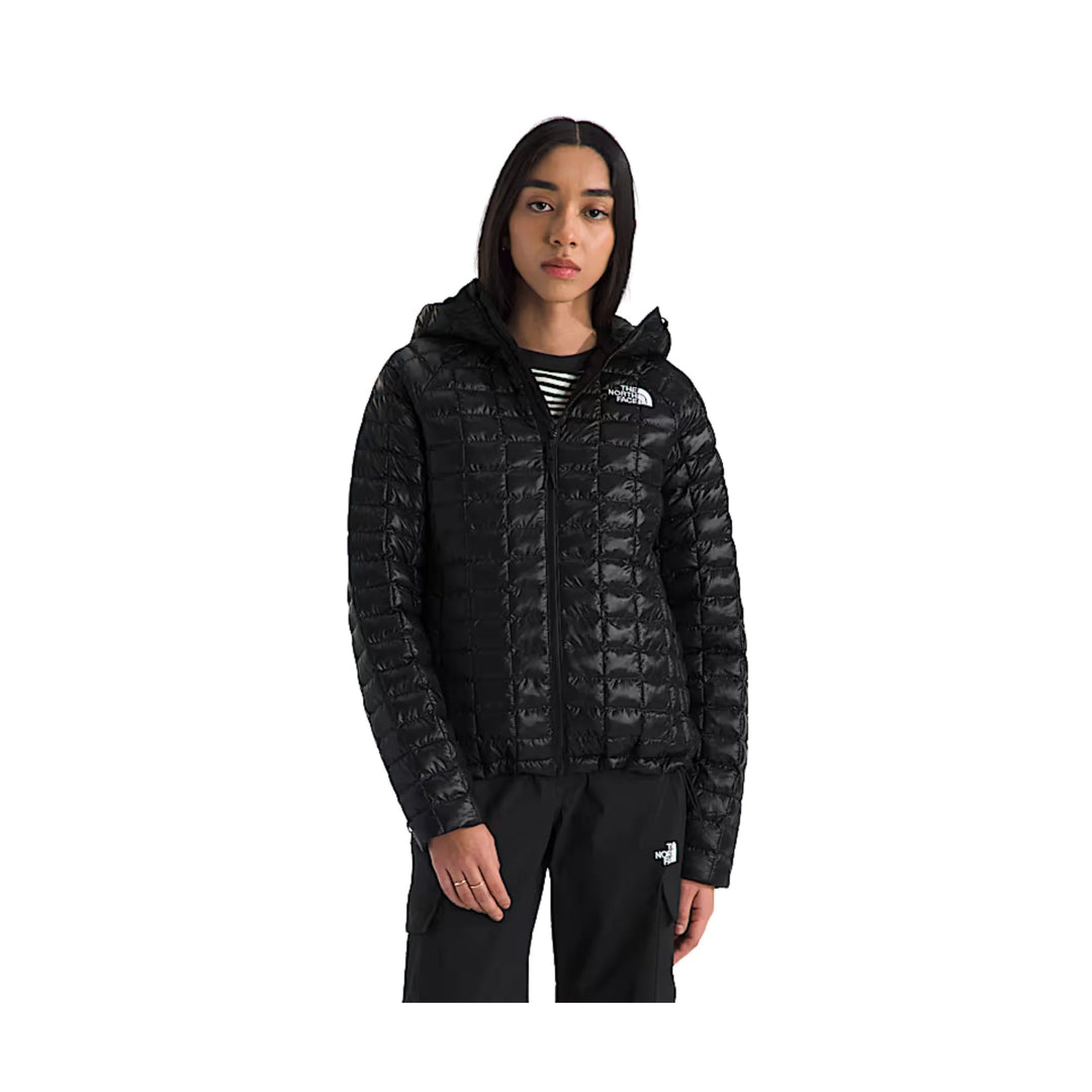 Black hooded quilted puffer jacket with front zipper and white chest logo, worn with black pants