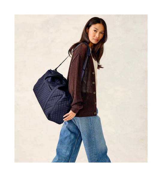 Quilted navy weekender bag with top handles and shoulder strap, worn over the shoulder
