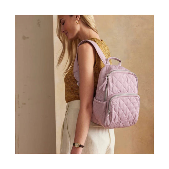 Light pink quilted small backpack with front zip pocket and top handle, worn on one shoulder