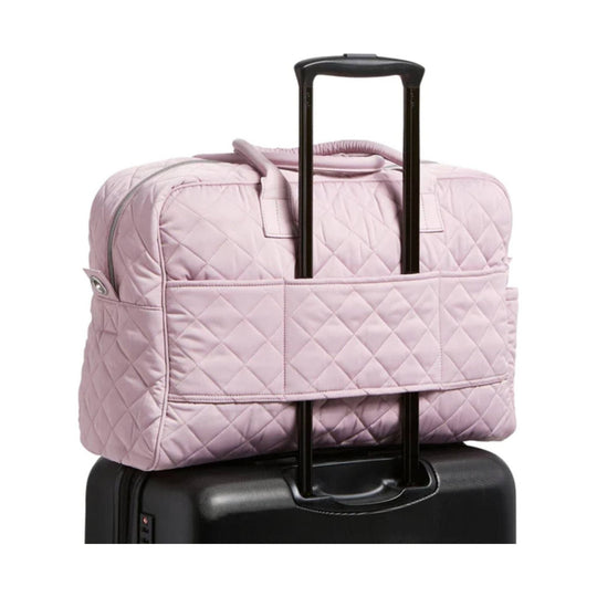 Light pink quilted travel bag with luggage sleeve over a black suitcase handle