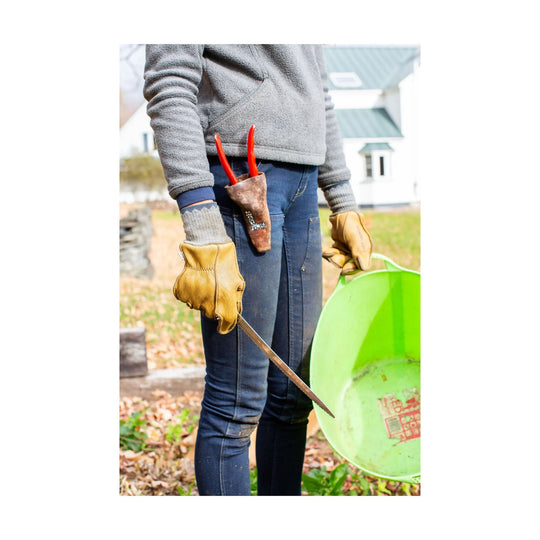 Pair of tan leather work gloves with red hang loops, shown with a folding pruning saw