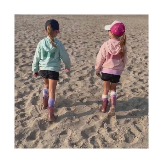 Sparkly rain boots on two children walking in sand, shown from the back