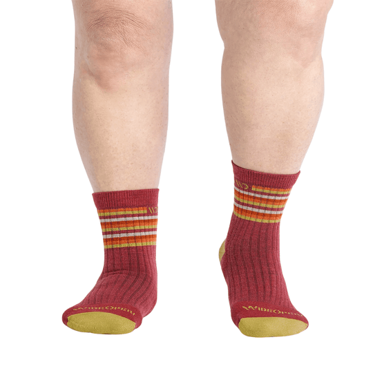 Pair of cranberry ankle socks with multicolor stripes and yellow soles on a model's lower legs