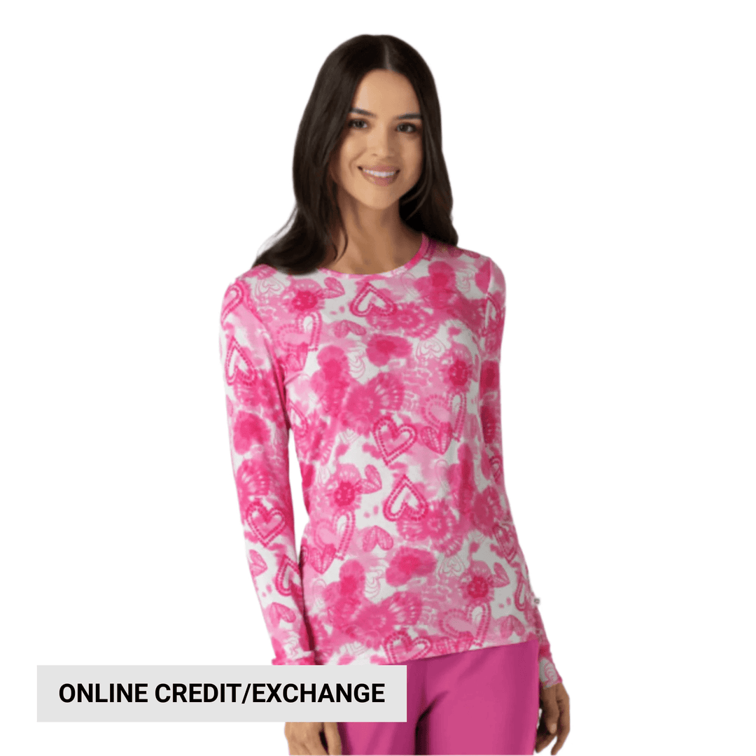 Pink and white long-sleeve scrub top with heart pattern on a model, with “ONLINE CREDIT/EXCHANGE” text overlay