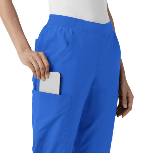 Blue cargo scrub pants with a ribbed waistband and large side pocket, shown on a model holding a phone.