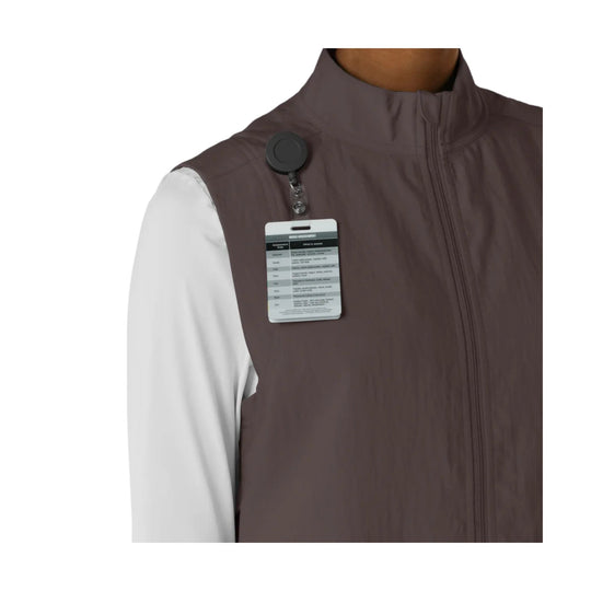 Brown zip-front scrub vest with a clipped assessment card at the chest