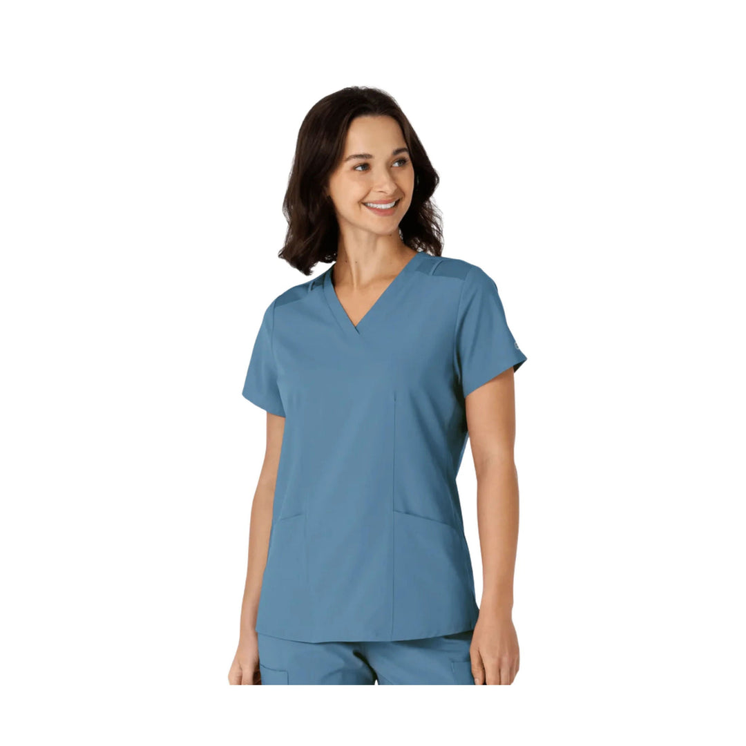 Blue V-neck scrub top with short sleeves and front patch pockets, shown on a model