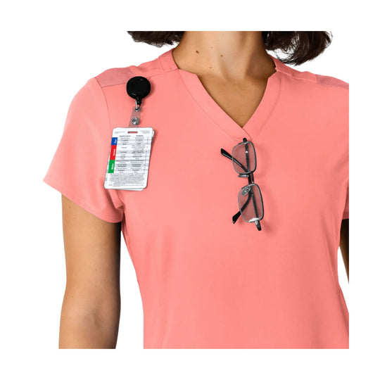 Coral V-neck scrub top with shoulder panels, clipped ID badge, and glasses hanging from the neckline