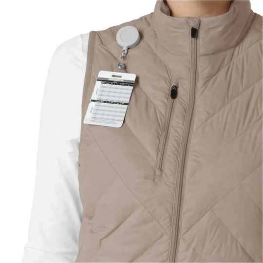 Beige quilted zip-front vest with a chest clip and hanging size tag over a white long-sleeve top